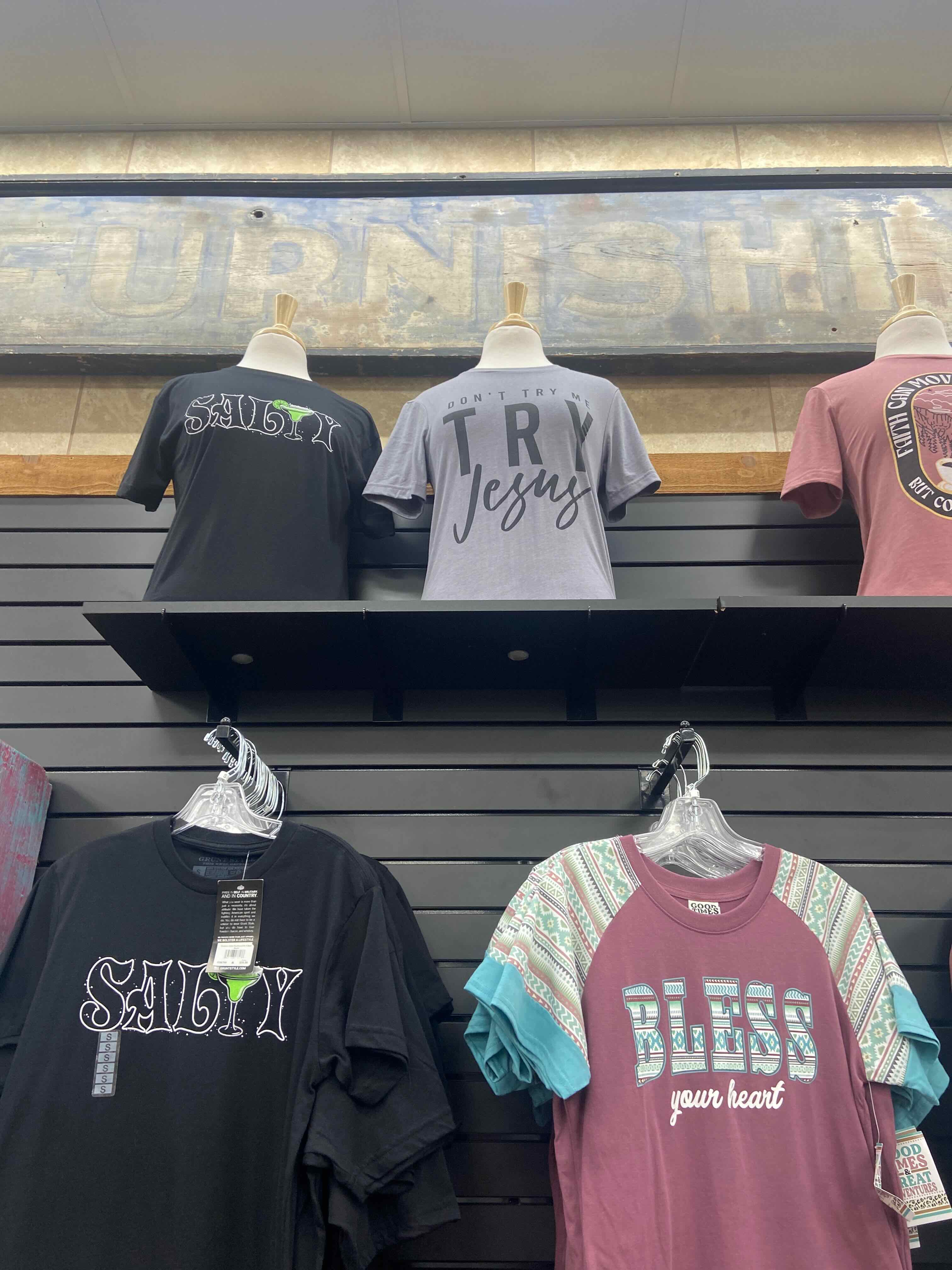 PHOTO: Shirt wall — "Don't Try Me, Try Jesus," "Salty" with martini, "Bless Your Heart"