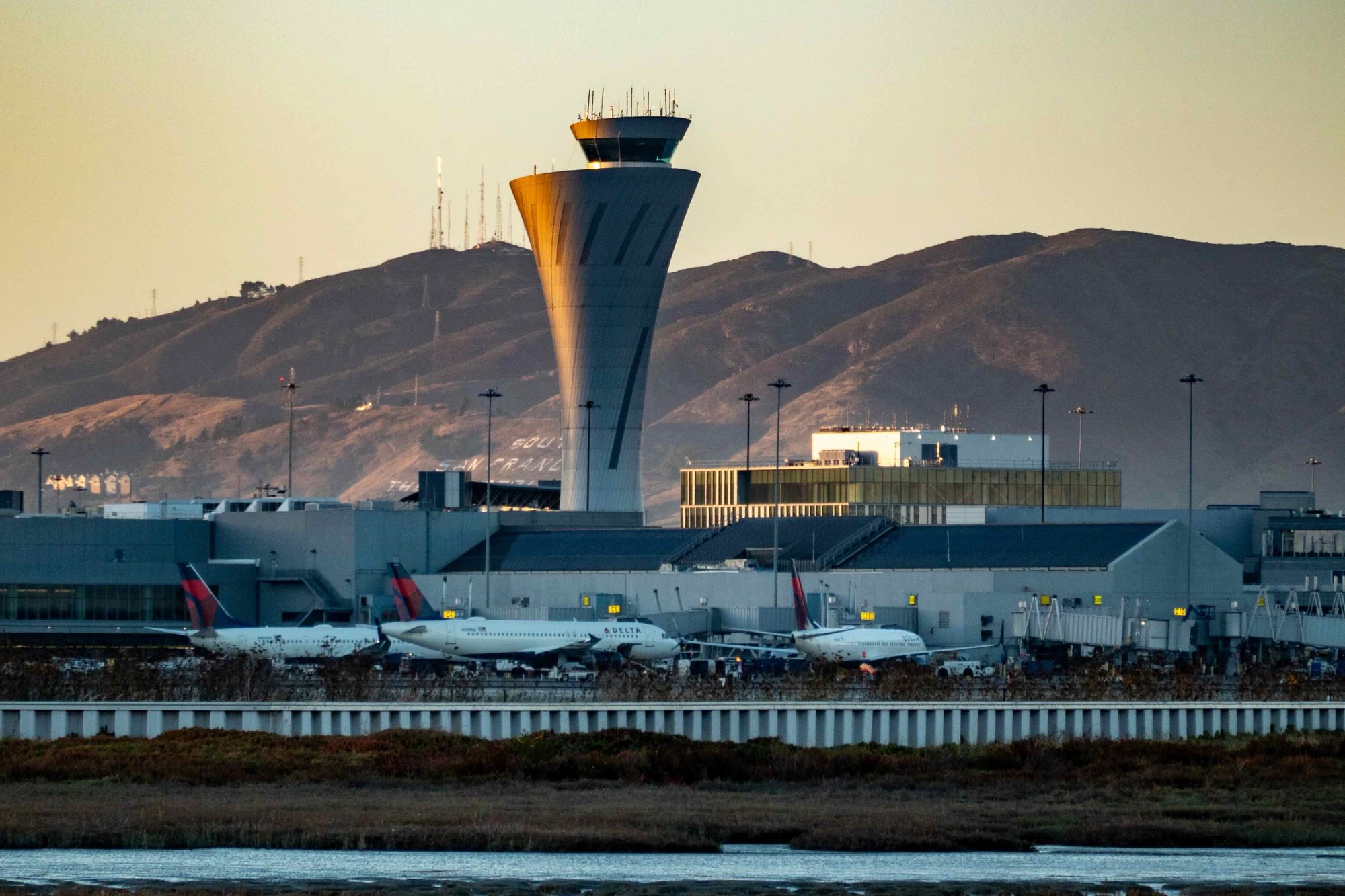 The control tower and a terminal at San Francisco International Airport at dusk, with Delta jets at the gates, seen across bayfront marsh