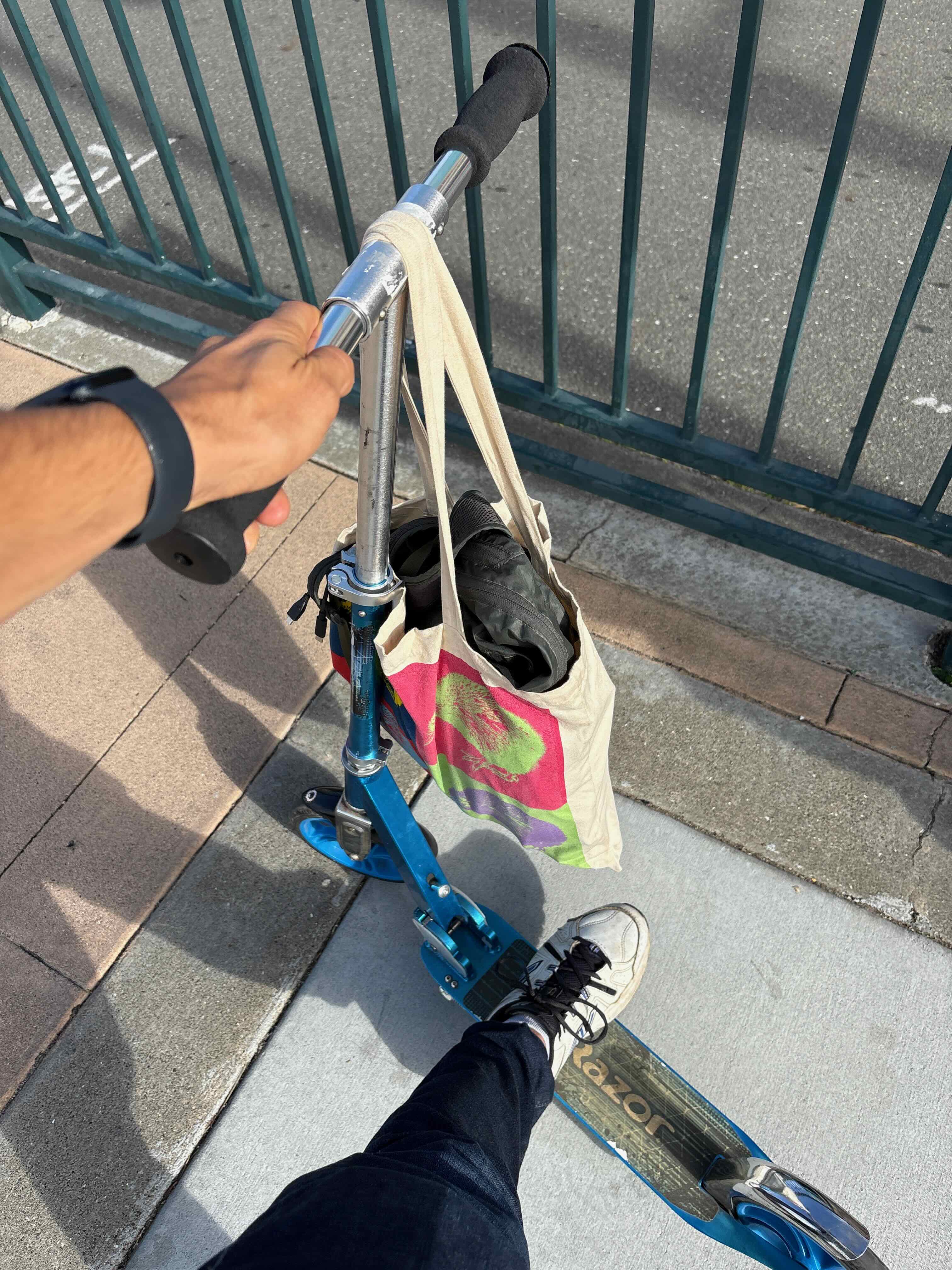 a kickscooter with a canvas bag hanging from its handlebars