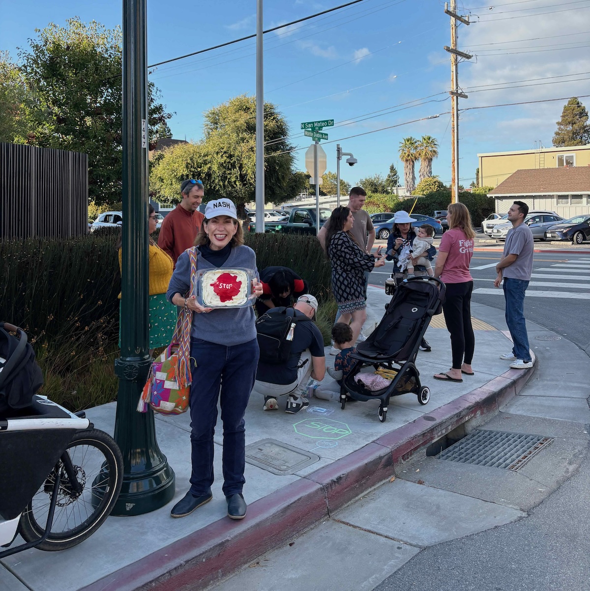 A councilmember holding the stop sign cake at the corner of North San Mateo Drive and Monte Diablo Avenue
