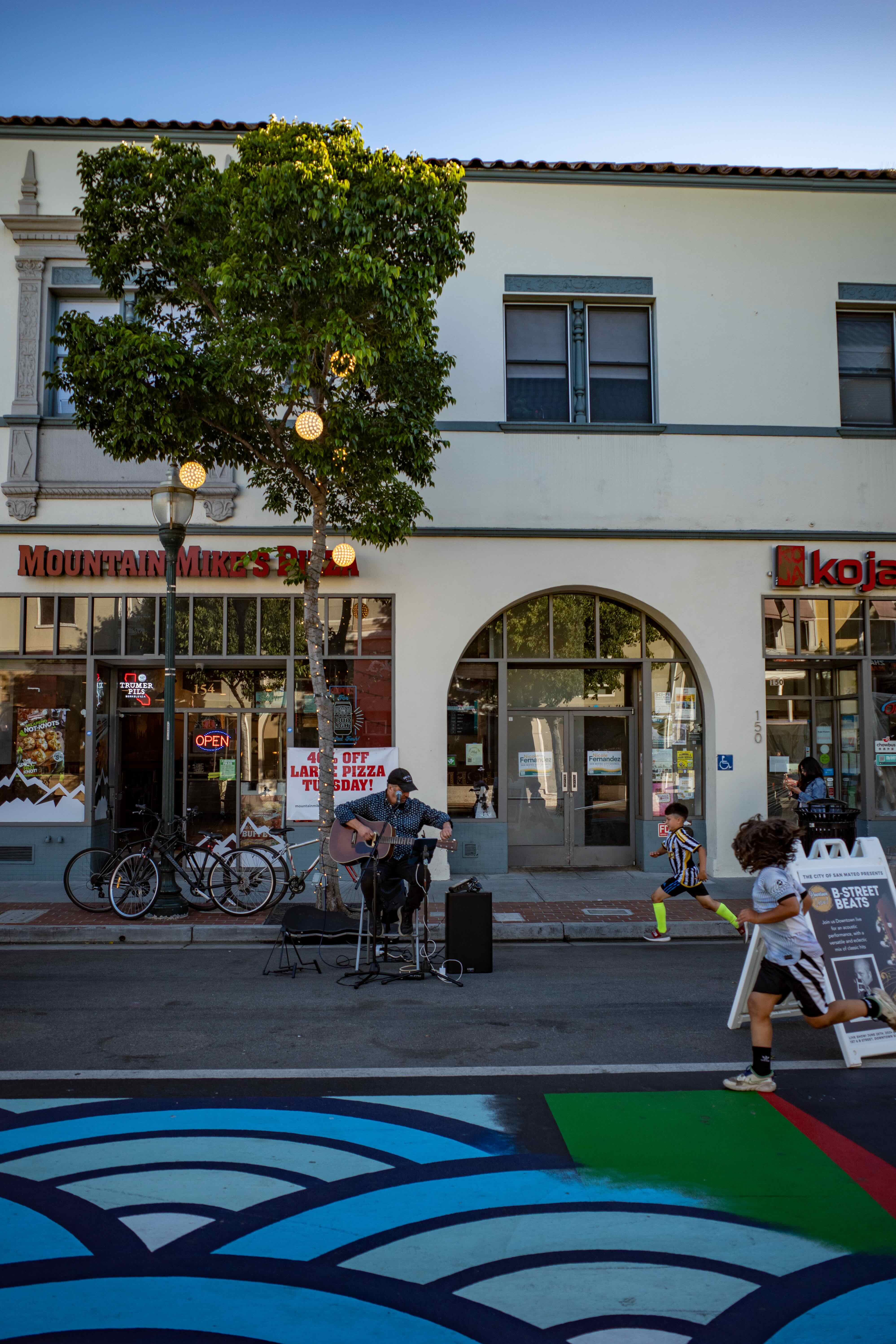 A street musician performing on B Street in San Mateo with two children running toward him