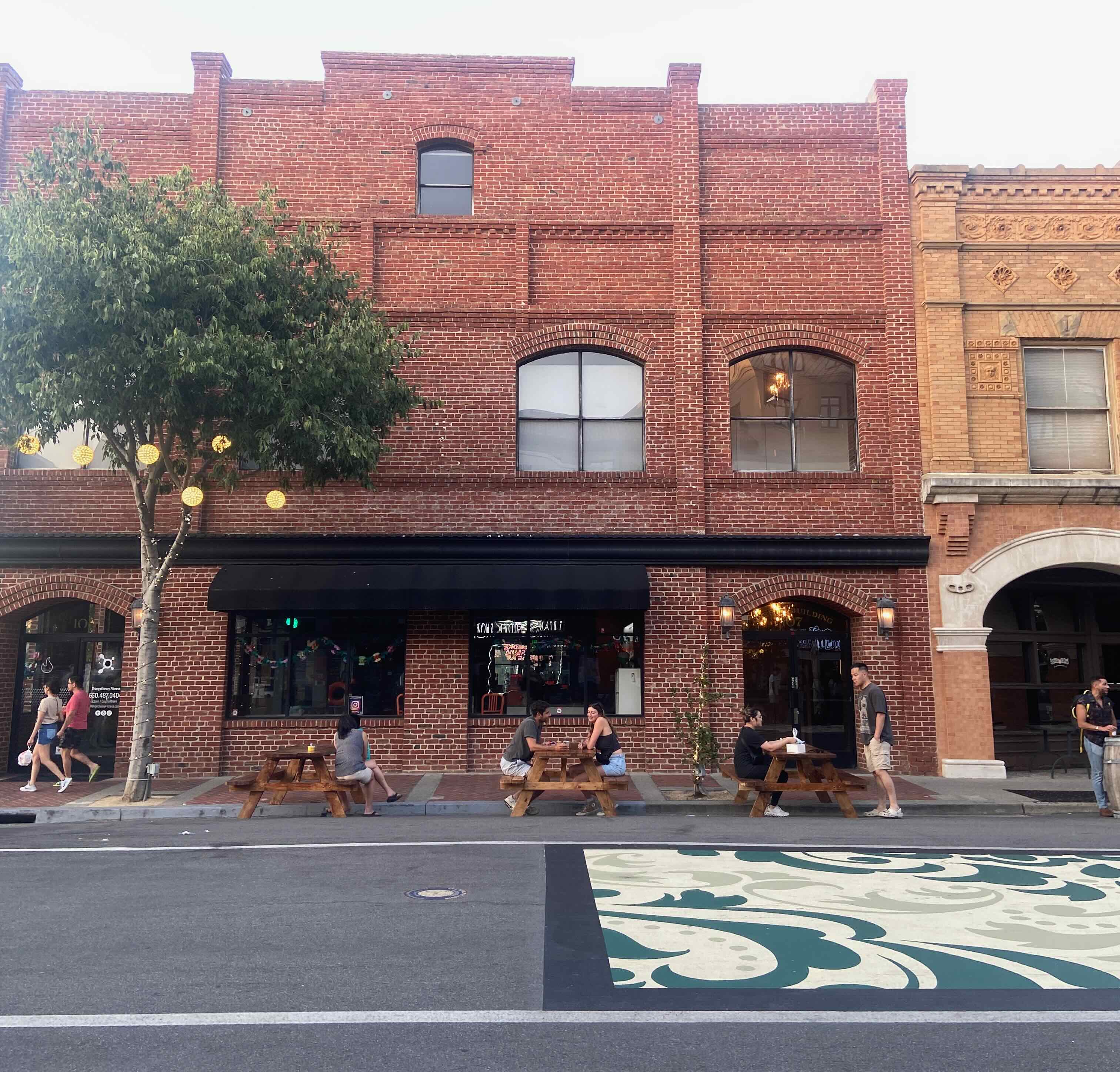 Three picnic tables on pedestrianized B Street in San Mateo, all occupied by people eating and socializing