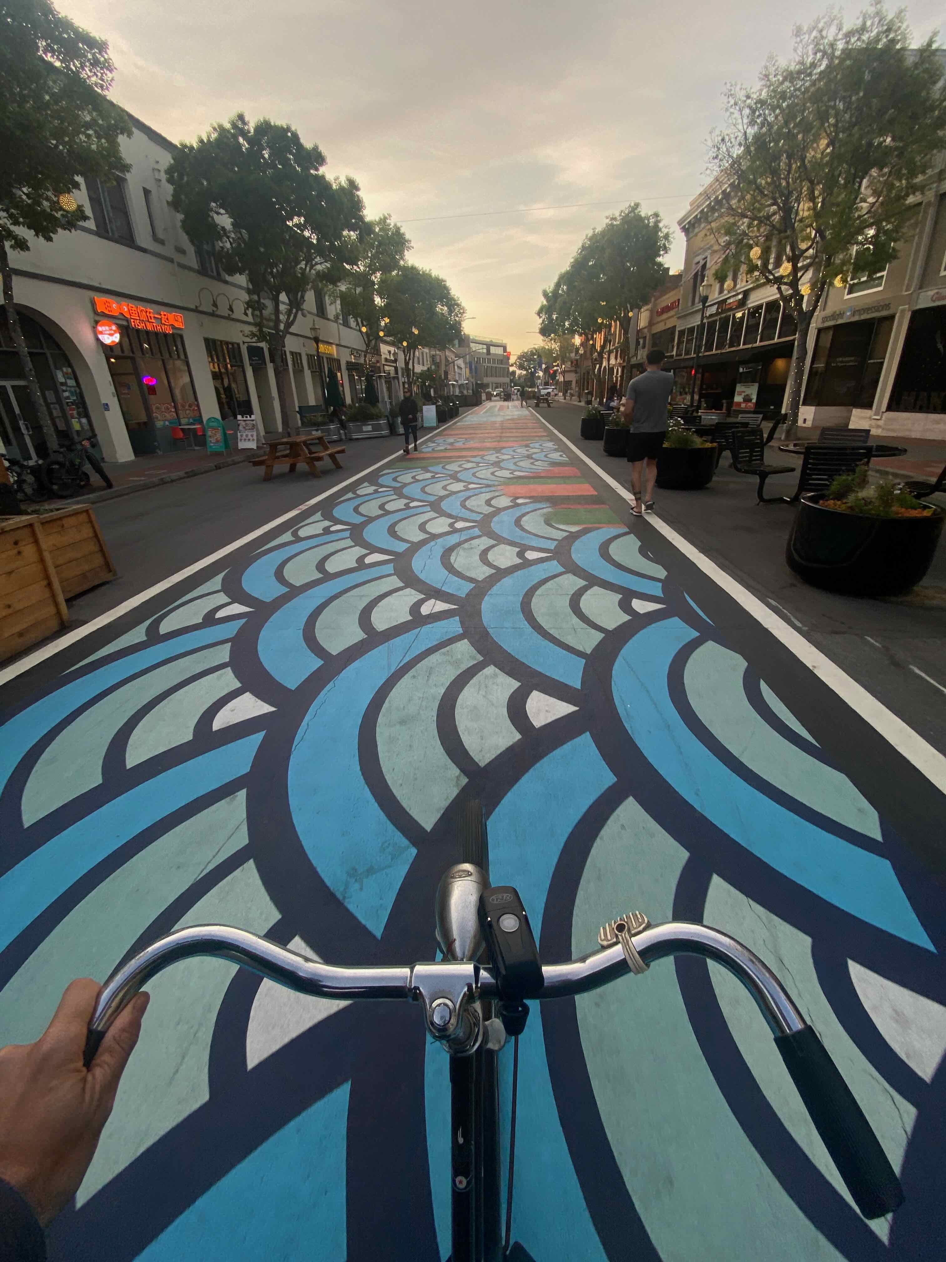 Point-of-view photo of bicycle handlebars over the painted street mural on B Street in San Mateo