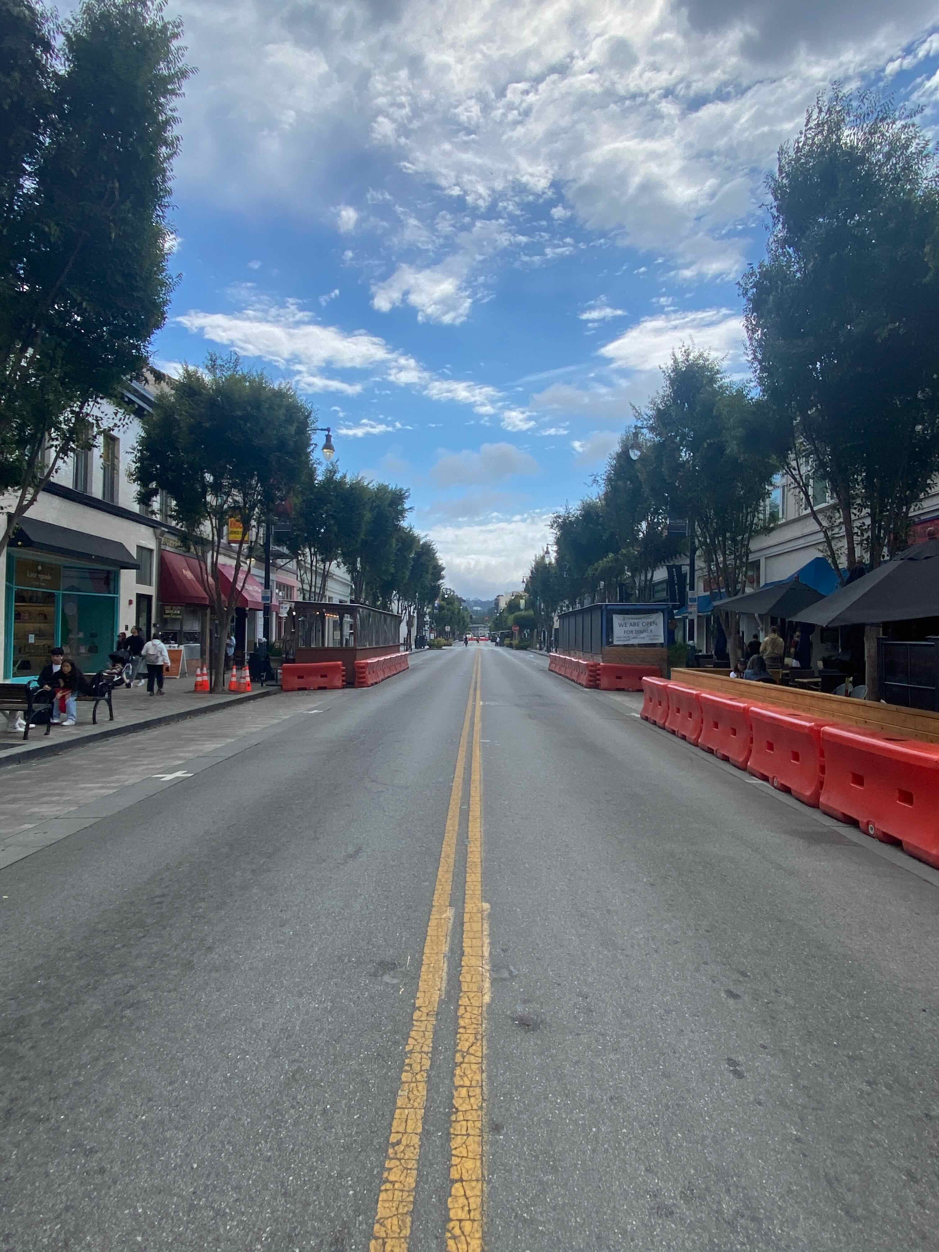 A pedestrian crossing in front of orange barriers closing Burlingame Avenue on a quiet weekday