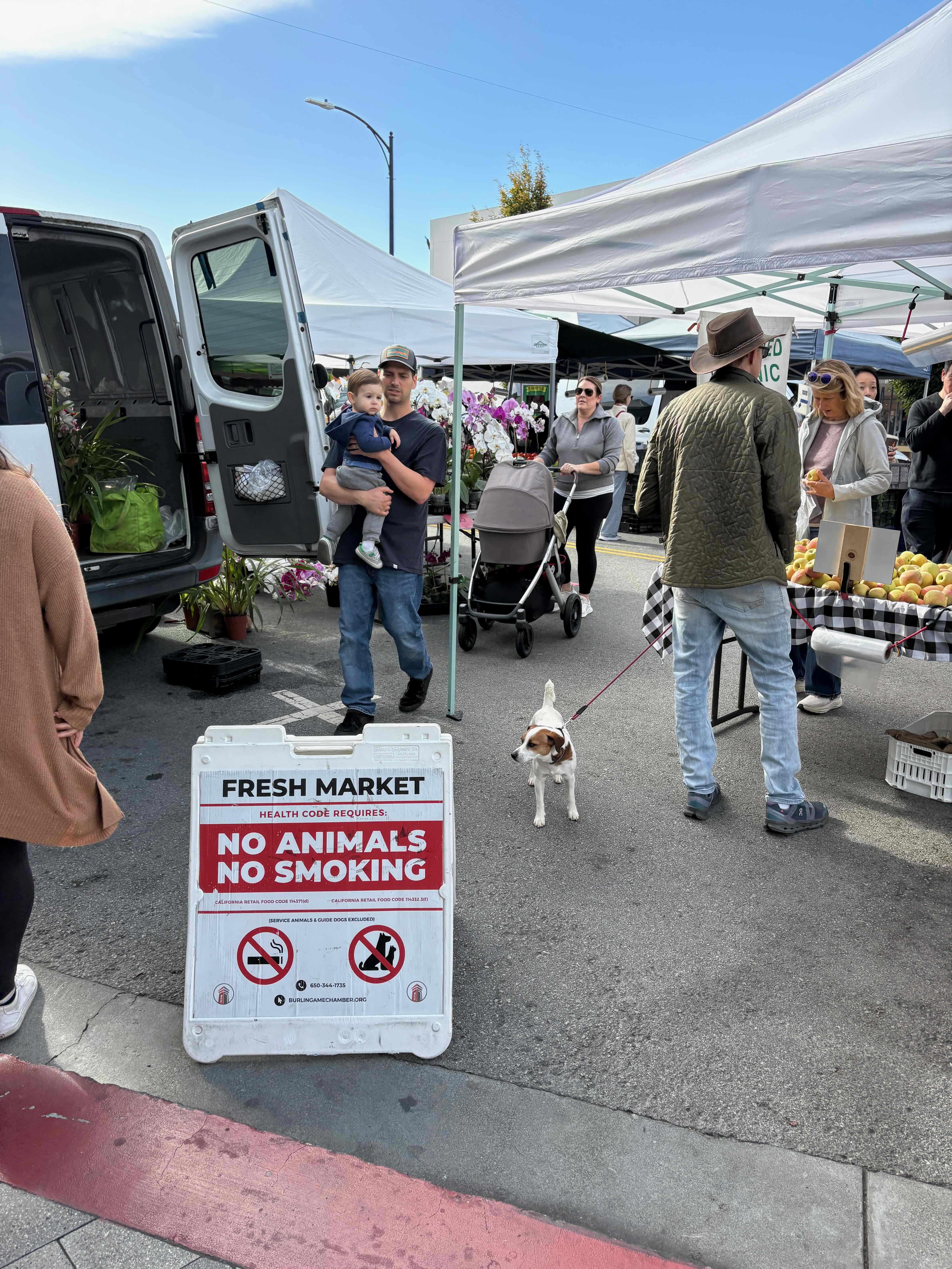 The Burlingame Farmers Market on Park Road with a 'No Animals' sign next to a dog on a leash