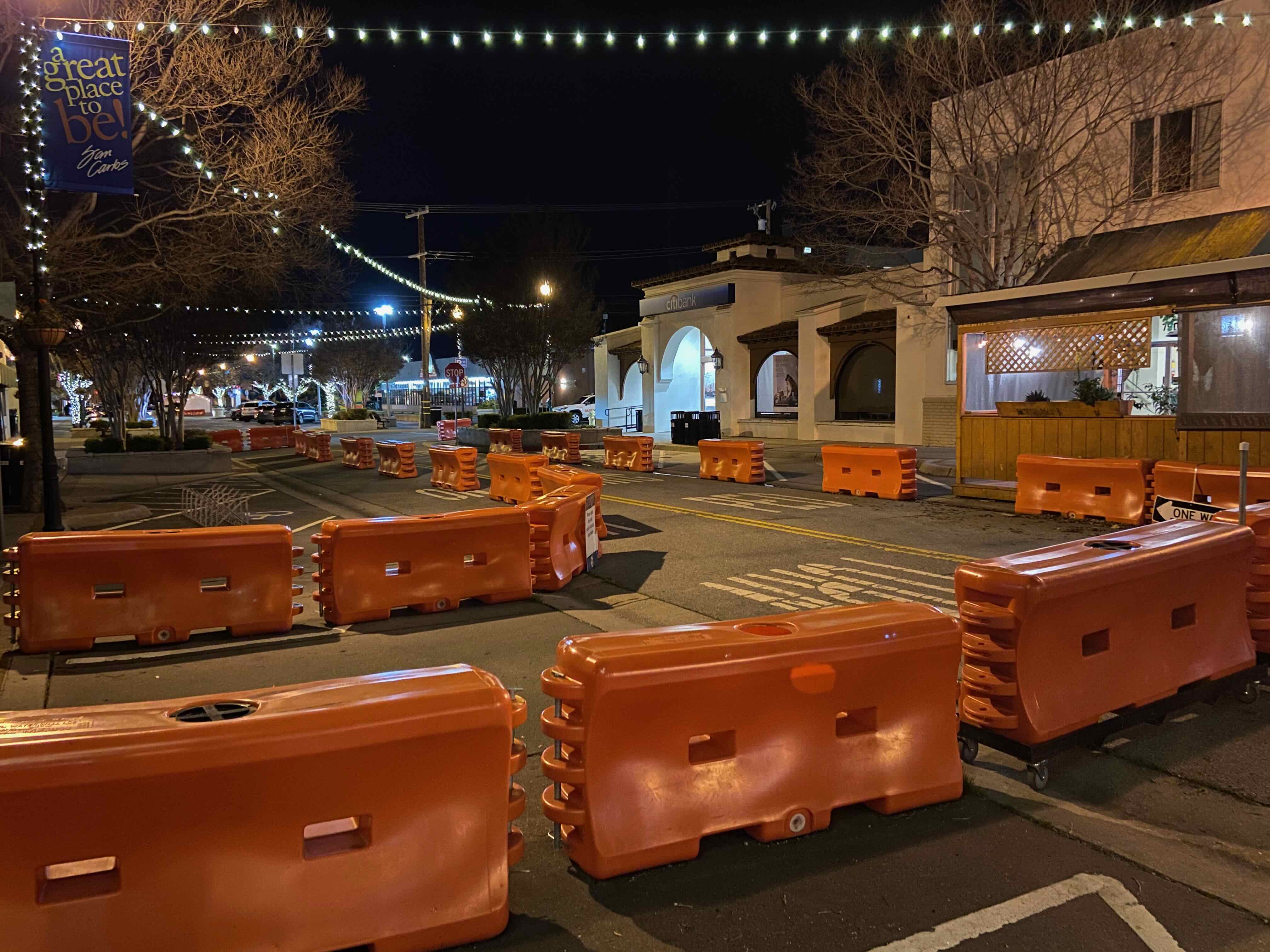Orange water barriers blocking Laurel Street in San Carlos at night with a "A Great Place to Be" banner overhead