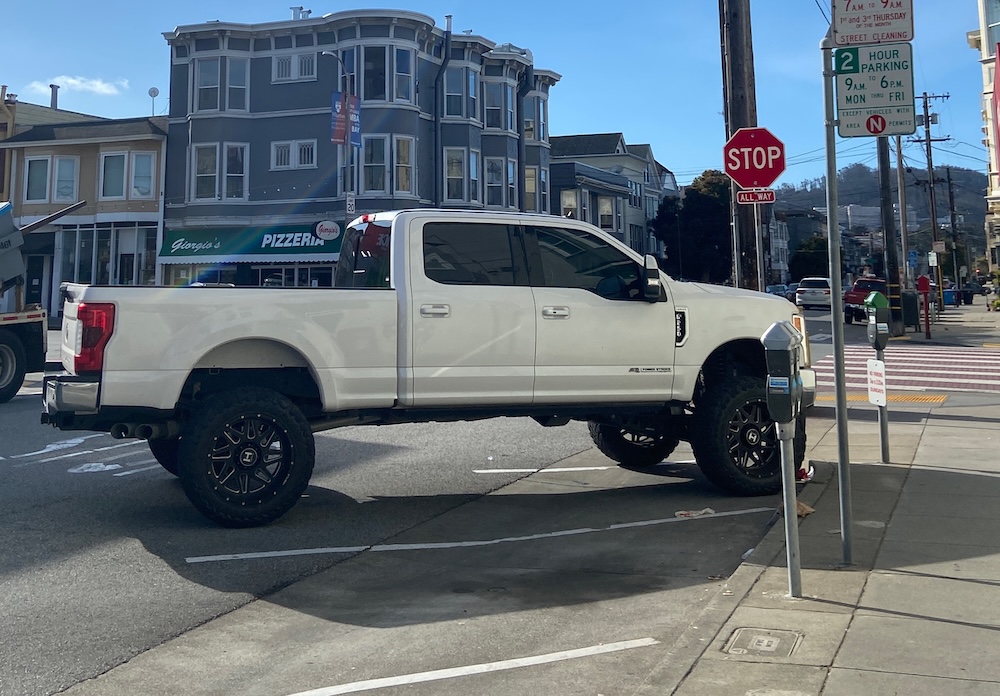 A Ford F-250 parked at a San Francisco corner, overhanging its stall and reaching the crosswalk, against a row of Victorian storefronts.