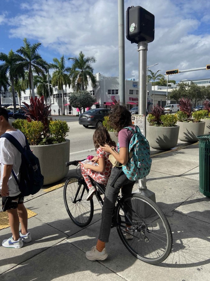 A child seated on the top tube between their mother's arms, reading a book